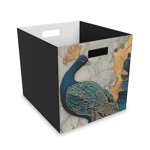 May include: A storage bin with a black exterior and a white interior. The front panel features a peacock design with blue, teal, and gold accents against a marble-like background. The bin has two handle cutouts.