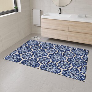 May include: A rectangular bathroom mat with a repeating floral pattern in shades of blue and white. The mat is placed on a tiled floor in front of a vanity. The mat's design features a symmetrical floral motif.