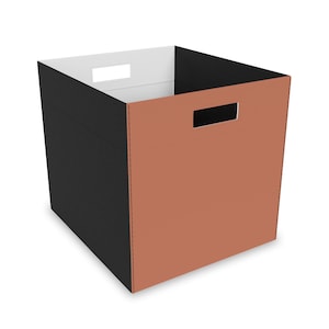 May include: A square storage bin with a two-tone design. The exterior features a black and copper color scheme, with a white interior. The bin has rectangular cut-out handles on two sides.