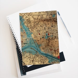 May include: A vintage map of a city with a river running through it. The map is printed on a light brown background with blue and red accents. The map is in a worn and faded condition, giving it a vintage look.