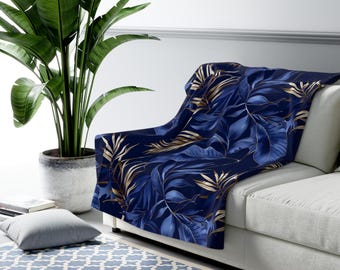 May include: A navy blue throw blanket with a gold leaf pattern. The blanket is draped over a white couch.