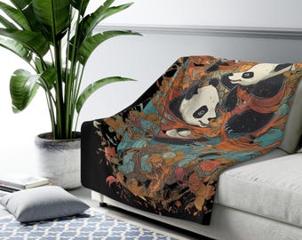 May include: A black blanket featuring a colorful illustration of two pandas. The pandas are surrounded by orange, blue, and brown floral designs. The blanket is draped over a white couch, with a large green plant in the background.