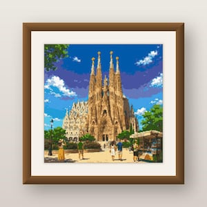 May include: A framed pixel art print depicting the Sagrada Familia in Barcelona. The scene features the tan stone cathedral under a bright blue sky with white clouds, surrounded by green trees and several small figures walking in the plaza.