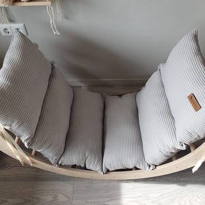 May include: A wooden rocking chair with a gray waffle-textured cushion. The cushion is made up of four separate pieces, each with a different shape. The chair is made of natural wood and has a simple design.
