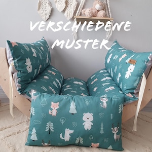 Könnte beinhalten: Eine hölzerne, halbmondförmige Schaukel mit tealfarbenen und weißen gemusterten Kissen. Die Kissen zeigen verschiedene Tier- und Naturmotive. Der Text "VERSCHIEDENE MUSTER" ist auf der Schaukel sichtbar.