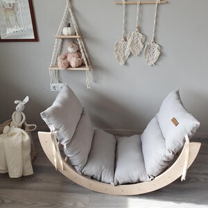May include: A wooden rocking chair with a gray and white striped cushion. The chair is made of natural wood and has a curved shape. The cushion is made of soft fabric and has a comfortable design.