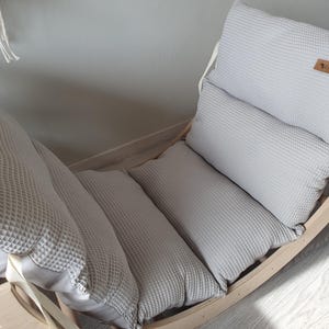 May include: A wooden rocking chair with a gray waffle-textured cushion. The cushion is made up of three separate pieces, and the chair has a white strap.