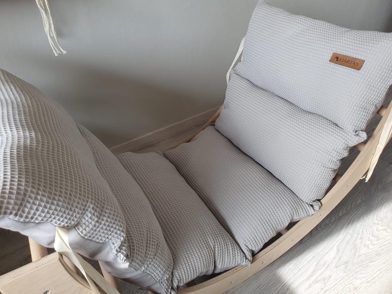 May include: A wooden rocking chair with a gray waffle-textured cushion. The cushion is made up of three separate pieces, and the chair has a white strap.