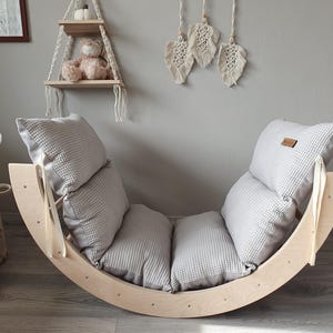 Könnte beinhalten: Ein Holz-Schaukelstuhl mit einem grauen gepolsterten Sitz. Der Stuhl ist aus Naturholz gefertigt und hat ein schlichtes, modernes Design.