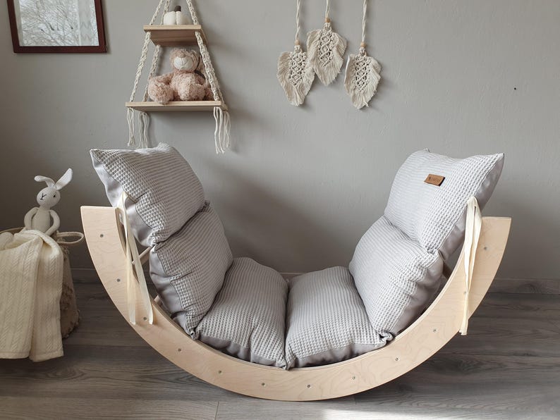 May include: A wooden rocking chair with a gray cushioned seat. The chair is made of natural wood and has a simple, modern design.
