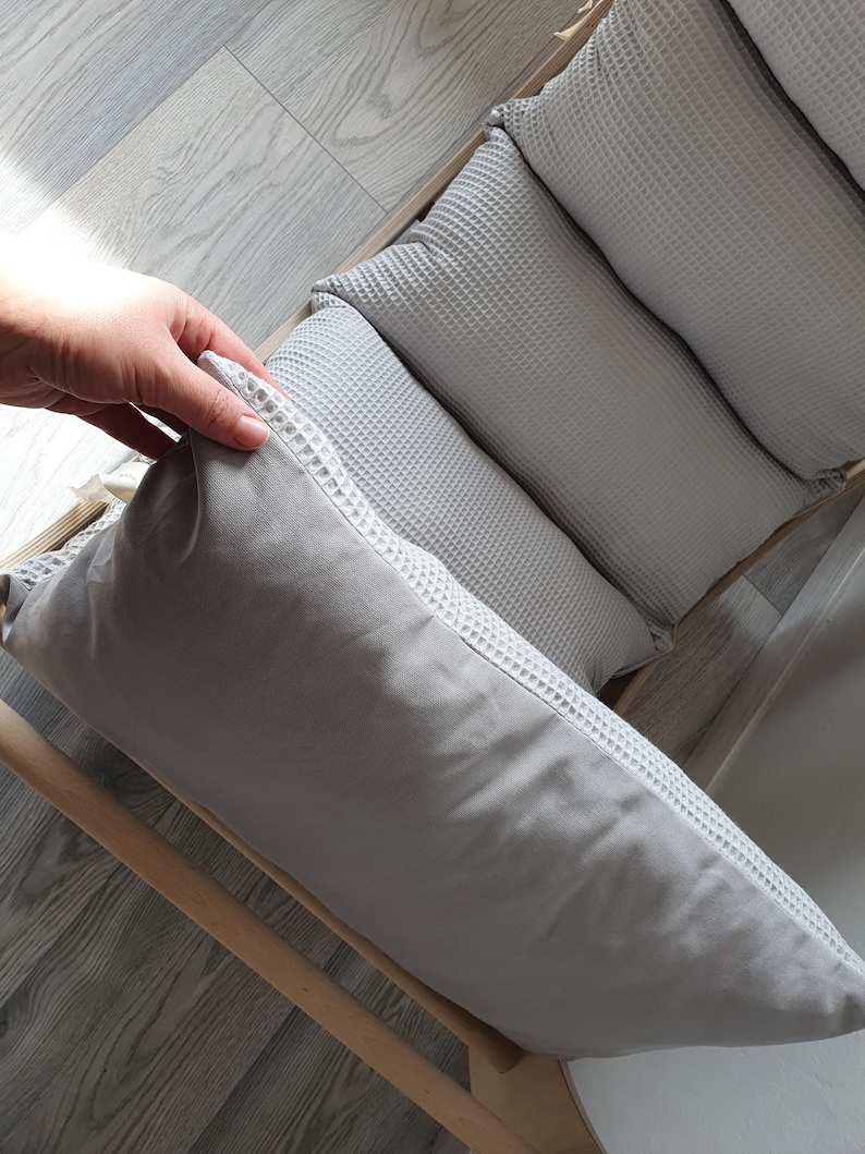 May include: A set of four gray waffle-textured cushions, arranged in a row on a wooden frame. The cushions are soft and comfortable, and would be perfect for a couch or bed.