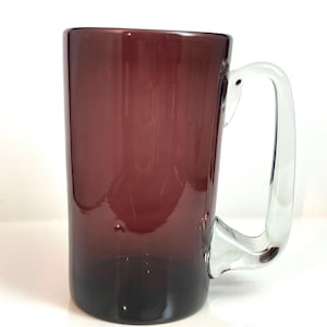 May include: A large, clear glass mug with a dark purple tinted body and a clear glass handle.