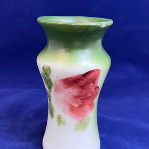 May include: A white glass vase with a green and white ombre effect. The vase is decorated with a hand-painted pink rose and green leaves.