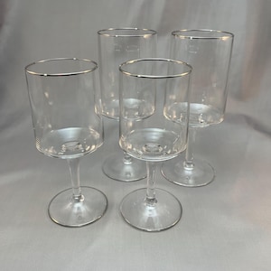 May include: Set of four clear glass wine glasses with a silver rim.