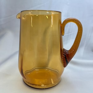 May include: Amber glass pitcher with a twisted handle. The pitcher has a wide mouth and a rounded base.