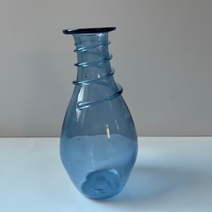 May include: A blue glass vase with a unique, twisted design. The vase has a rounded bottom and a narrow neck.
