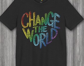 May include: Dark gray t-shirt with the words "CHANGE THE WORLD" in a rainbow-colored heart design. The words "Can You" are incorporated into the design. The shirt is made of a soft material.