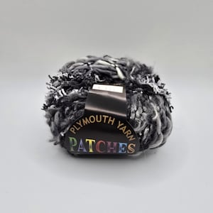 May include: A ball of Plymouth Yarn Patches in shades of gray, black, and white. The yarn has a textured, fluffy appearance. The label is black with the brand name and product name in white and rainbow colors.