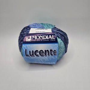 May include: A ball of Lucente yarn from Mondial, in shades of blue and teal. The label reads "Made in Italy" and includes the brand name and yarn type. The yarn is a blend of wool and cotton.