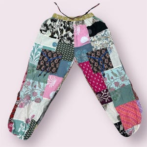 May include: Patchwork pants with a variety of floral and geometric patterns in shades of pink, blue, green, and brown. The pants have a drawstring waist and a gathered elastic at the ankles.