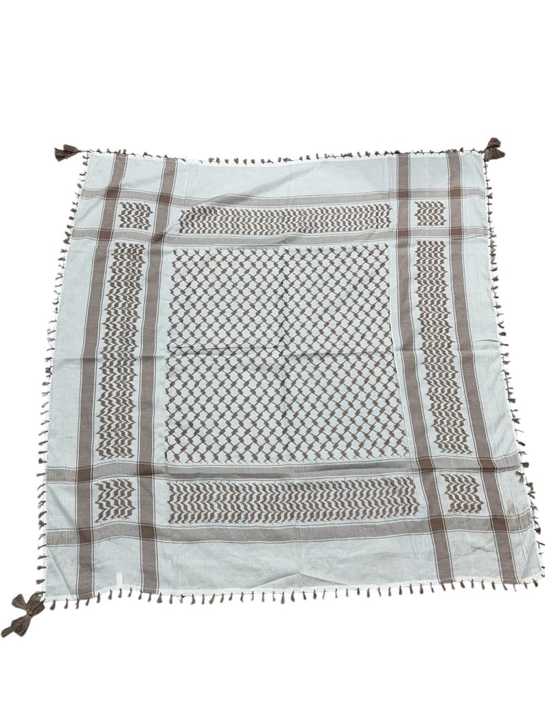 May include: A square, off-white scarf with a brown geometric pattern and fringe. The scarf features a repeating diamond and zigzag design, with brown stripes along the edges and tassels at each corner. The scarf is made of a soft, lightweight material.