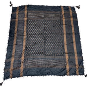May include: A black and tan keffiyeh scarf with a geometric pattern. The scarf has a diamond and striped design, with tassels on each corner. The scarf is made of a soft material.
