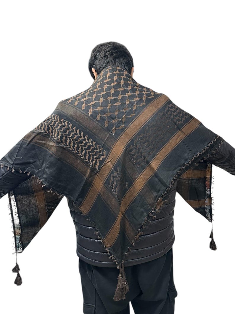 May include: Black and brown keffiyeh scarf with a geometric pattern and tassel trim. The scarf is draped over the shoulders. The scarf has brown stripes and a repeating pattern.