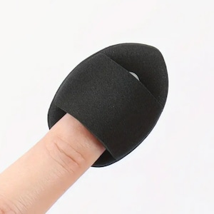 May include: Black makeup sponge with a hole for a finger, designed for blending makeup.