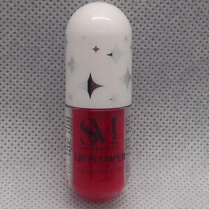 May include: A red lip plumper in a clear tube with a white cap. The cap has a silver star design and the text "SM Beauty" and "Lip Plumper" is printed on the tube.