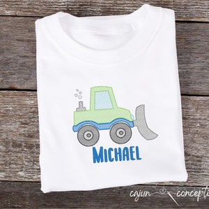 May include: A white t-shirt with a green and blue embroidered image of a toy bulldozer with the name "MICHAEL" embroidered below it.