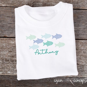 May include: White t-shirt with a design of blue and green fish swimming in a row. The name "Anthony" is written in green cursive below the fish.