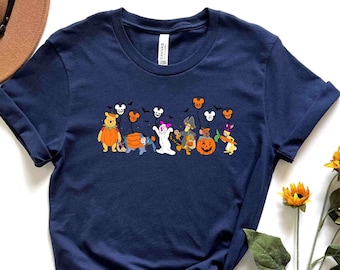 Może przedstawiać: Koszulka w kolorze granatowym z grafiką przedstawiającą postacie Disneya ubrane w kostiumy na Halloween. Postacie to Myszka Miki, Minnie Mouse, Donald Duck, Goofy, Pluto i Winnie the Pooh. Grafika jest umieszczona centralnie na koszulce i przedstawia postacie trzymające dynie i słodycze.