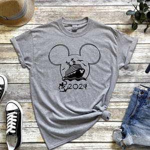 Op de afbeelding: Een grijs T-shirt met een zwart Mickey Mouse-hoofd ontwerp met een cruiseschip in de oren en de tekst "2024" eronder.