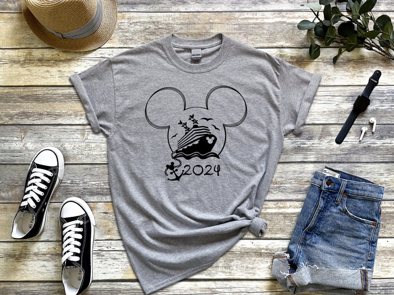Op de afbeelding: Een grijs T-shirt met een zwart Mickey Mouse-hoofd ontwerp met een cruiseschip in de oren en de tekst "2024" eronder.