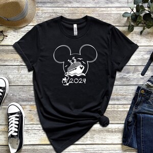 Op de afbeelding: Zwart T-shirt met een wit Mickey Mouse-kopontwerp met een cruiseschip in de oren en de tekst "2024" eronder.