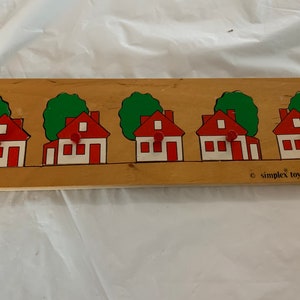 May include: A wooden puzzle featuring five red houses with white windows and green trees. The puzzle is made by Simplex Toys and says "made in Holland" on the bottom.