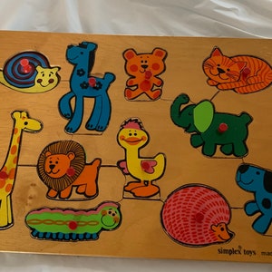 May include: A wooden puzzle featuring colourful animal pieces, including a giraffe, lion, elephant, cat, duck, and snail. The puzzle is made by Simplex Toys and is made in Holland.