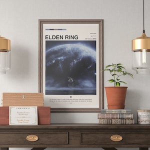 May include: A framed poster with the title "ELDEN RING" and a blue and white image of a character standing on a cliff overlooking a stormy sea. The poster is hanging on a white wall above a wooden table with a wooden box, a potted plant, a stack of books, and a candle.