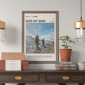 K&ouml;nnte beinhalten: Ein gerahmtes Poster mit dem Titel "God of War" und dem Erscheinungsdatum "20. April 2018". Das Poster zeigt eine Videospielszene mit zwei Charakteren, die durch eine schneebedeckte Landschaft gehen. Das Poster h&auml;ngt an einer Wand &uuml;ber einem Holztisch mit einer Topfpflanze, B&uuml;chern und einer Kerze.