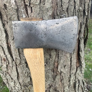 May include: A vintage axe with a wooden handle and a metal head. The head is weathered and has a gray patina. The handle is made of light wood and has a smooth finish.
