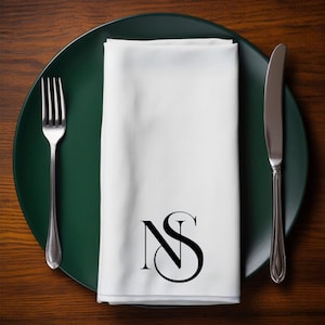 Può includere: Un tovagliolo di lino bianco con il monogramma "NS" in nero su un piatto verde con una forchetta e un coltello d'argento.