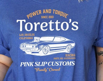 May include: A blue t-shirt with a white graphic design featuring a vintage car, the text "Power and Torque Since 2001 Toretto's Los Angeles California", and the text "Racing Party and Accessories Pink Slip Customs "Family" Owned".
