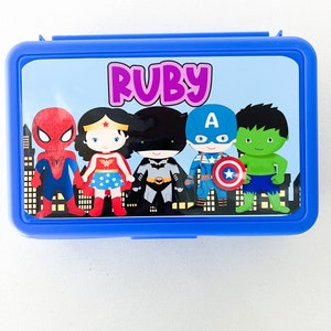 May include: A rectangular blue plastic lunch box featuring a custom graphic on the lid. The design displays the name Ruby in purple text above cartoon illustrations of Spider-Man, Wonder Woman, Batman, Captain America, and the Hulk.
