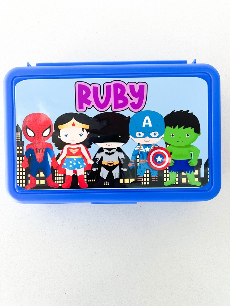 May include: A rectangular blue plastic lunch box featuring a custom graphic on the lid. The design displays the name Ruby in purple text above cartoon illustrations of Spider-Man, Wonder Woman, Batman, Captain America, and the Hulk.