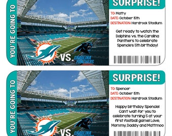May include: Two blue and green tickets with the text "You're going to" on the left side. The tickets feature a photo of a football stadium with the text "Surprise!" and "VS. Carolina Panthers" on the right side. The top ticket is for Matty and the bottom ticket is for Spencer. Both tickets are for October 15th at Hardrock Stadium.