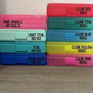 K&ouml;nnte beinhalten: Eine Sammlung von neun rechteckigen Kunststoff-Etuis, die in zwei Spalten gestapelt sind. Die Etuis sind mit ihren Farben und Abmessungen in Zoll beschriftet: Pink Sparkle 8x4.75x2.25, Light Teal, Teal, Royal Blue, Clear Red, Clear Teal, Clear Blue, Clear Yellow und Clear Pink 8x5x2.