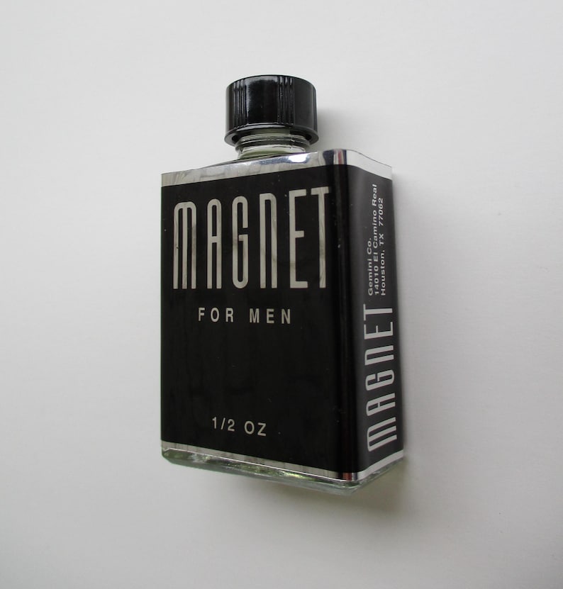 K&ouml;nnte beinhalten: Eine schwarze Glasflasche mit einem silbernen Etikett, auf dem "MAGNET FOR MEN 1/2 OZ" steht. Die Flasche hat einen schwarzen Verschluss und steht auf einem wei&szlig;en Hintergrund.