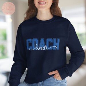 May include: A navy blue sweatshirt with the text "COACH lindi" in white and blue lettering.