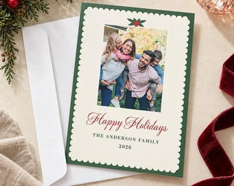 May include: A rectangular holiday greeting card with a scalloped cream border on a dark green background. The card features a central photograph of a family, a holly icon, and the red script text Happy Holidays, followed by The Anderson Family 2026.