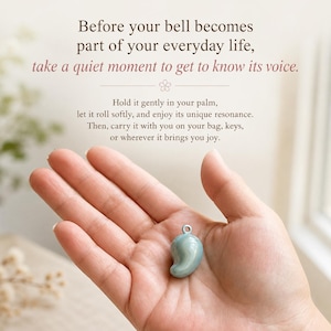 Może przedstawiać: Mały, gładki, jasnoniebieski dzwonek w kształcie kropli z metalowym k&oacute;łeczkiem na g&oacute;rze. Tekst głosi: Before your bell becomes part of your everyday life, take a quiet moment to get to know its voice. Hold it gently in your palm.